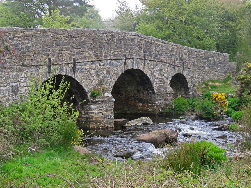 A stone bridge with three arches over a swiftly moving stream.