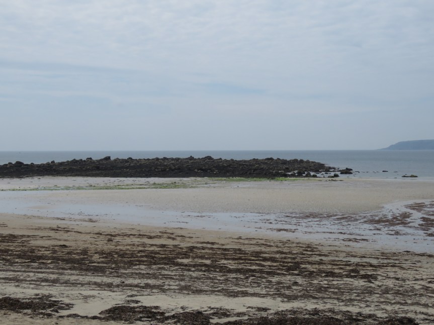 Rocks beyond a sandy beach at low tide.