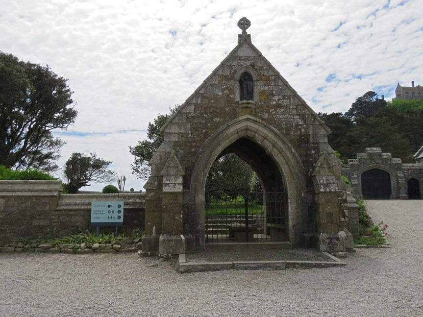 Stone archway with a metal gate at the end of a low stone wall.