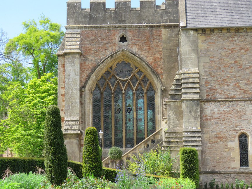 Stained glass arch window with topiaries in the foreground.