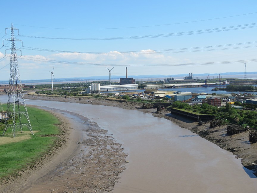View of a muddy river and some industrial buildings in the distance.